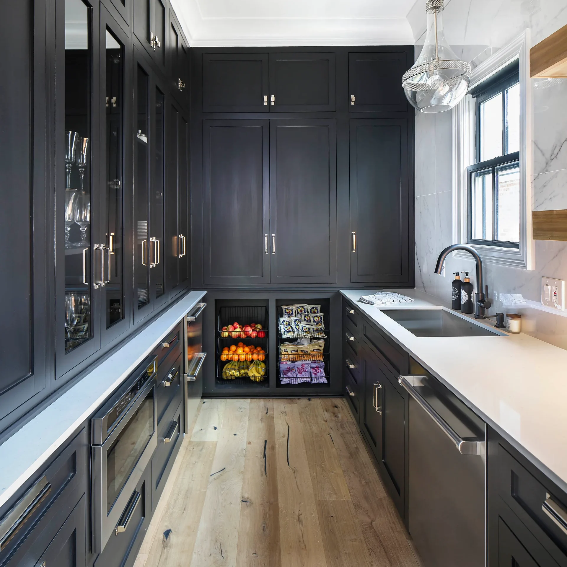 Narrow modern pantry with black cabinets, white counters, and a single glass pendant light.