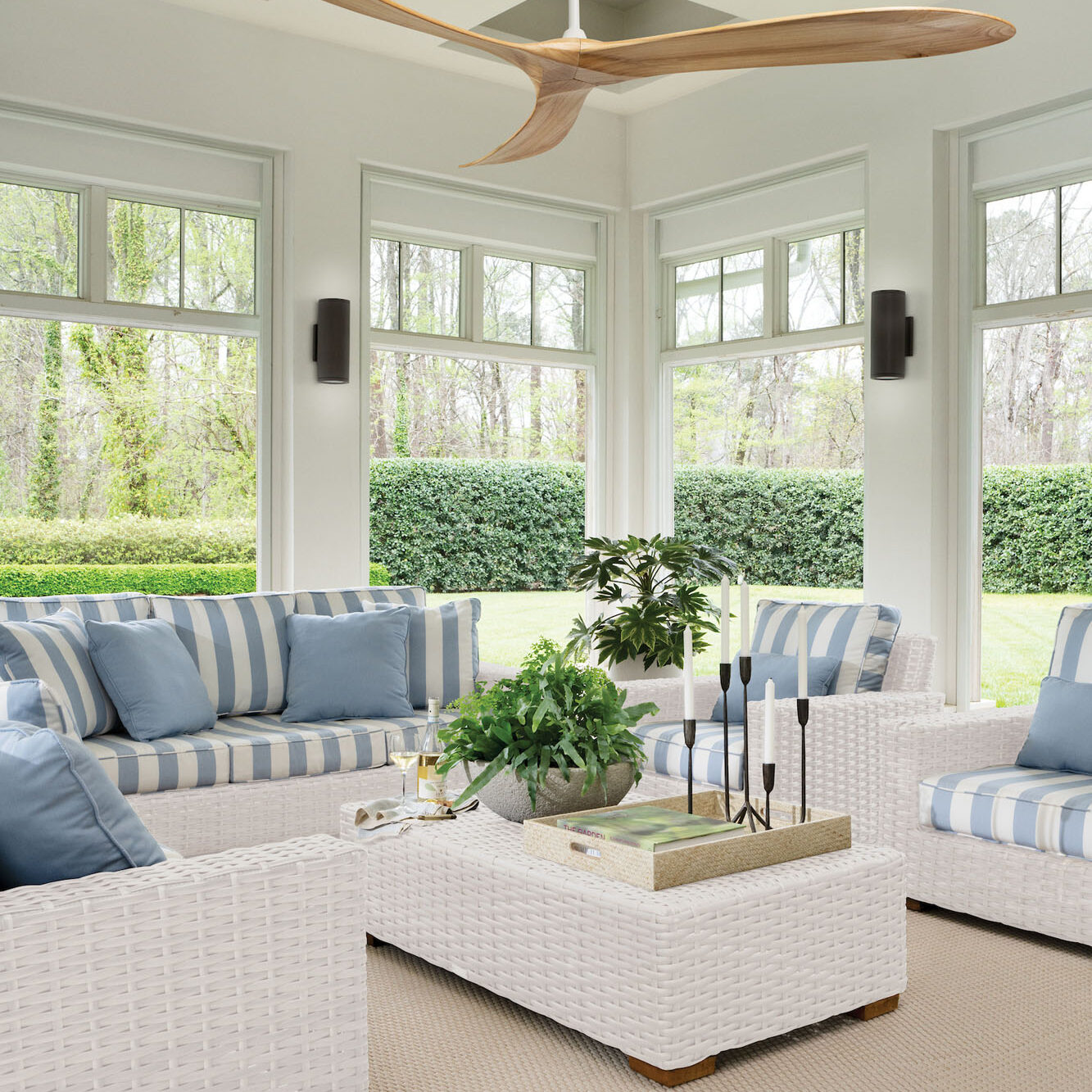 Sun-filled sunroom or porch with a built-in seating area dressed in light blue and white striped cushions, full of potted plants.