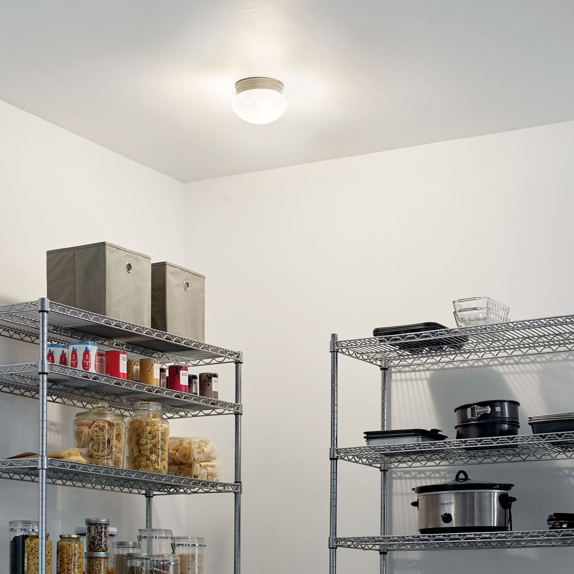 Simple, round ceiling light fixture illuminating a white pantry with chrome shelving.