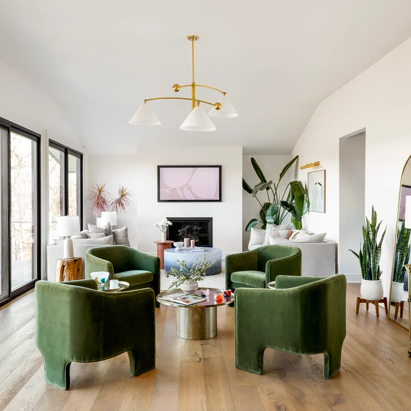 Bright living room with a white sectional, two green velvet armchairs, and a brass chandelier over a patterned rug.