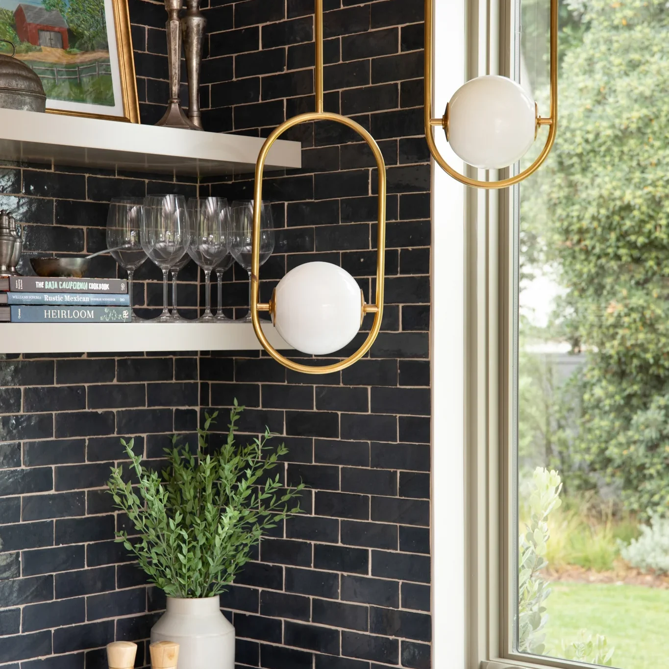 Two brass oval cage pendant lights with white globes over a black tile backsplash.