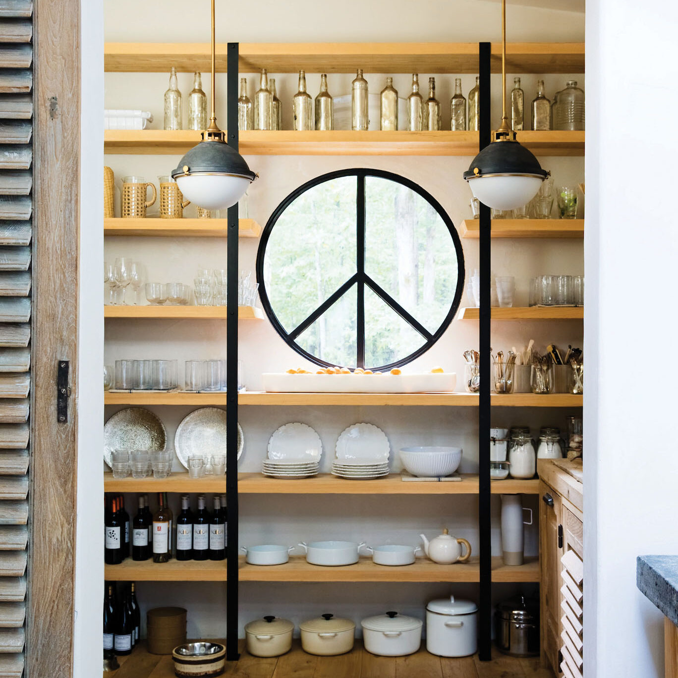 Open pantry with wood shelves, white dishes, and a round window with a peace sign design.