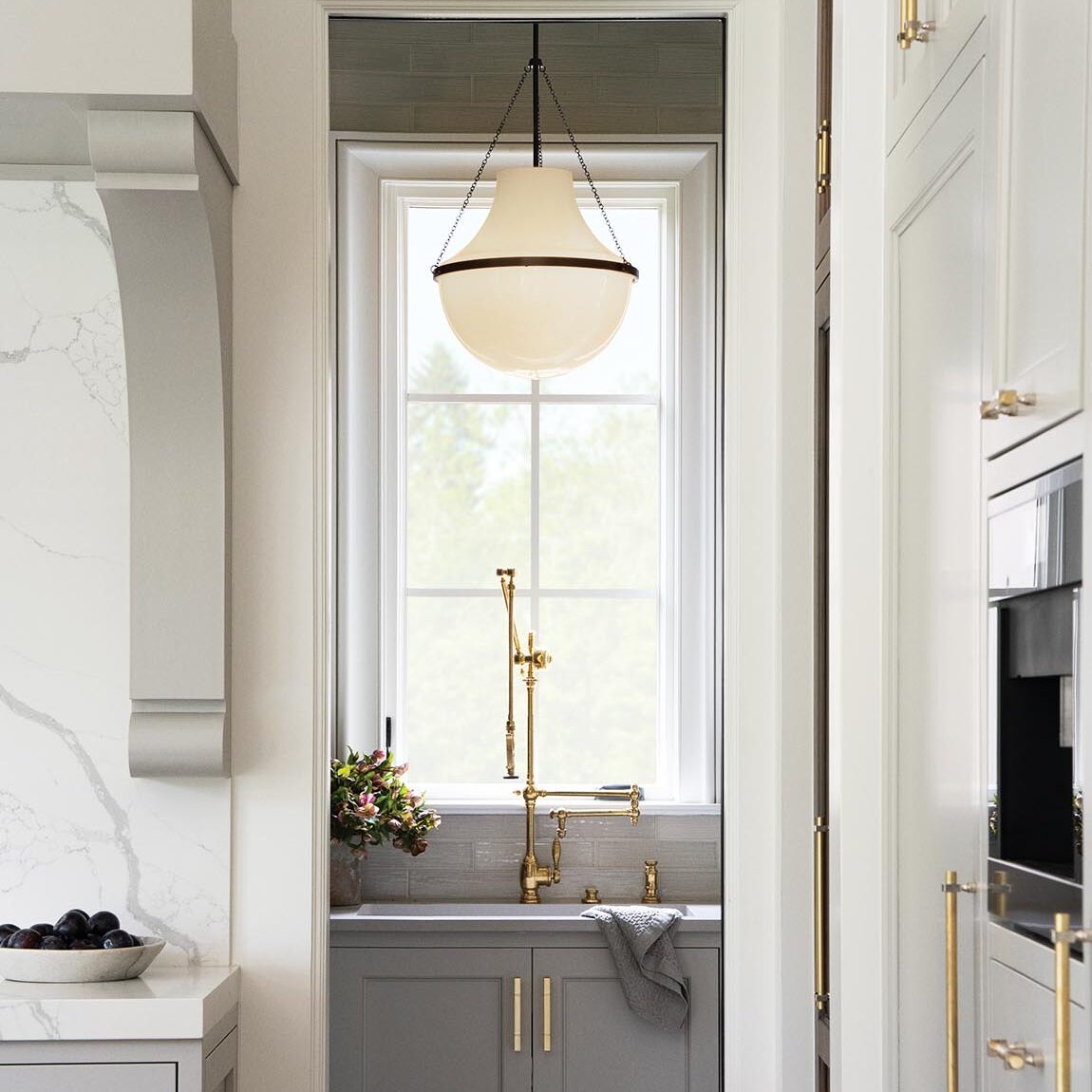 Large white glass globe pendant light hanging over a sink with a brass bridge faucet.