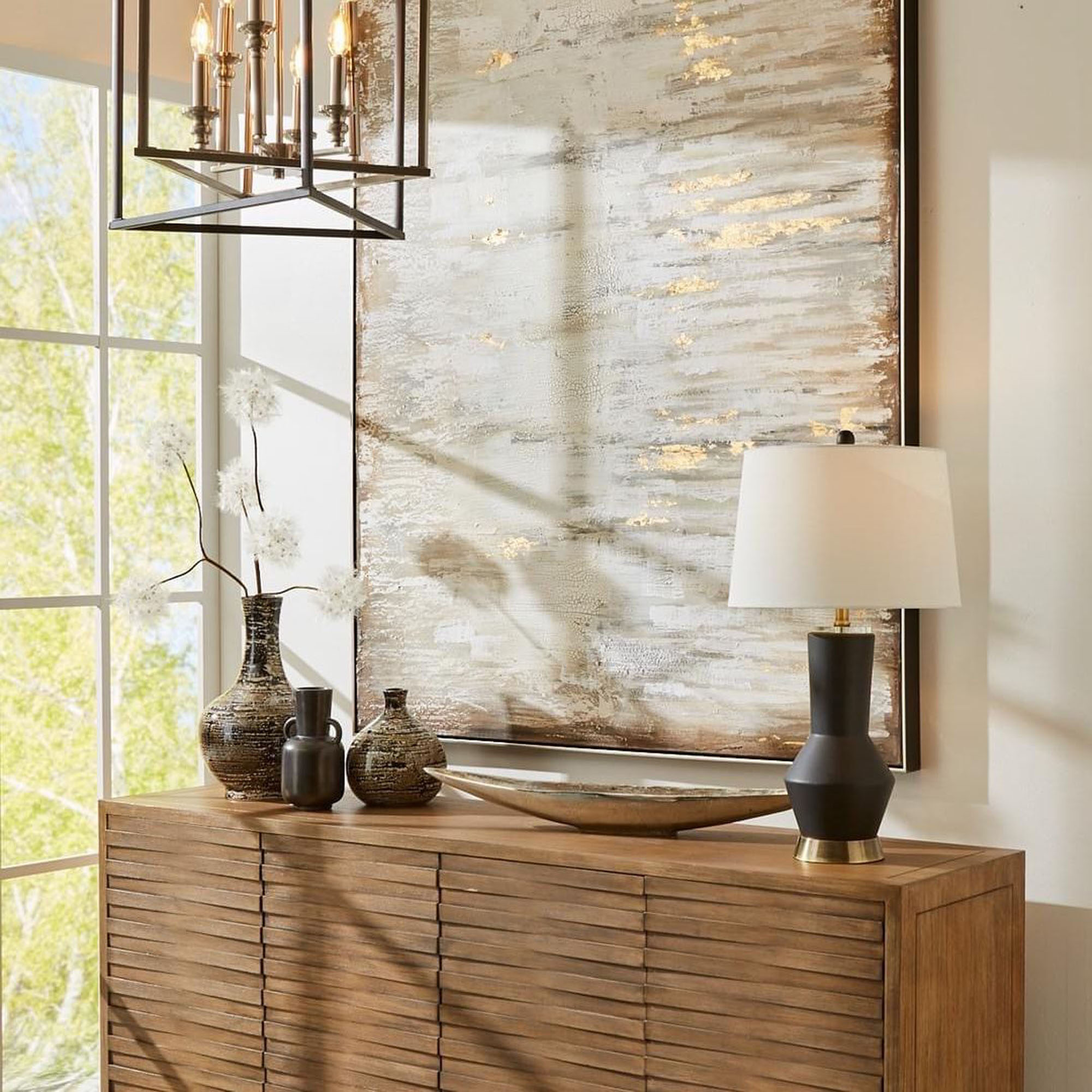 Entryway or sideboard featuring a textured wood cabinet, large decorative bowl, black table lamp, and an industrial-style multi-bulb chandelier.