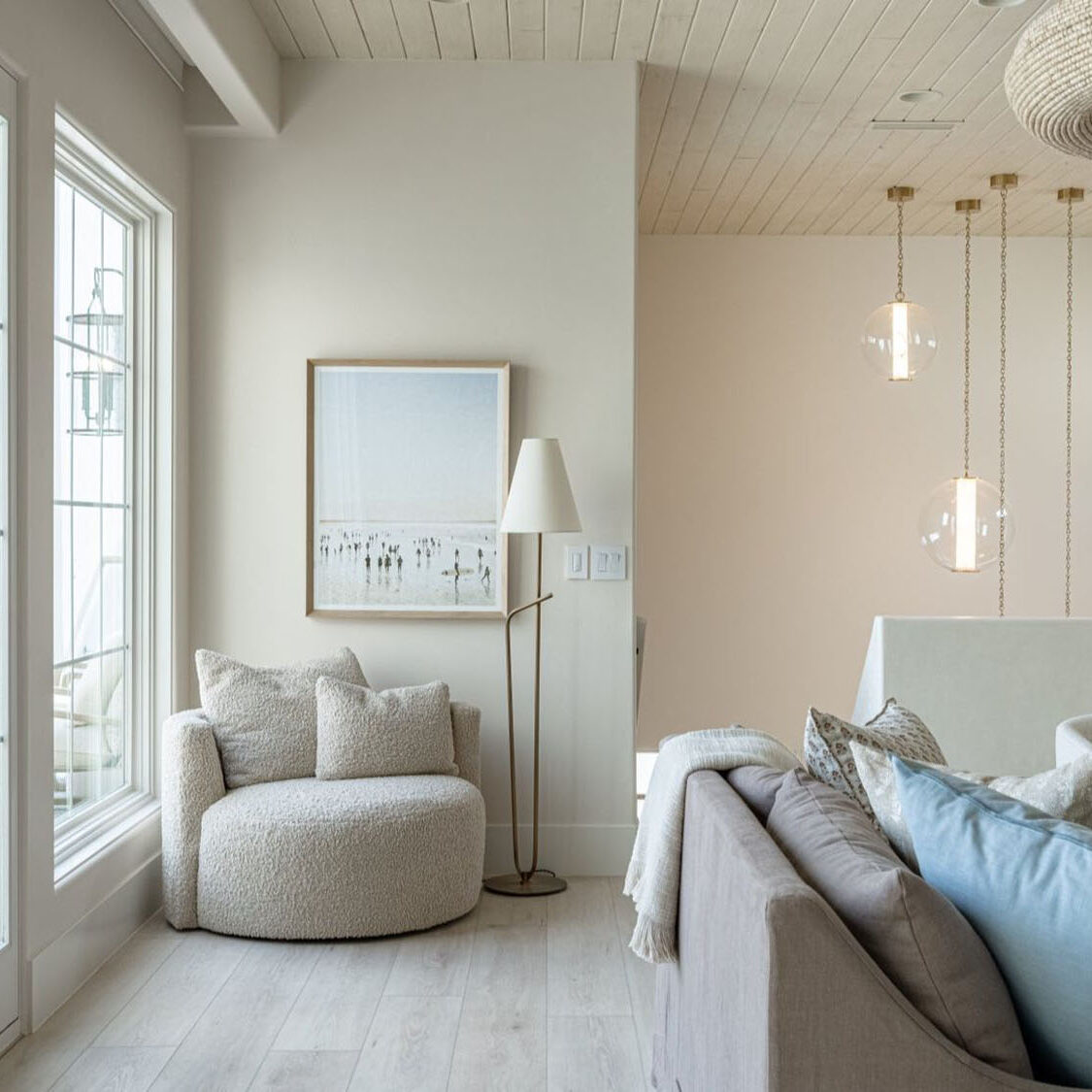 Serene, monochromatic room with a small round ottoman, a delicate cluster of pendant lights, and a framed mirror above a low cabinet.