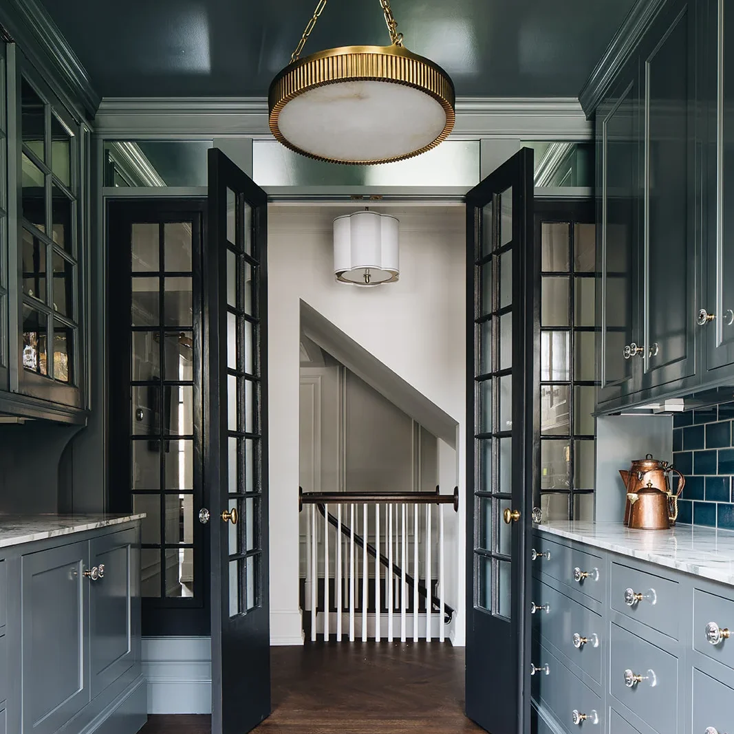 Large circular gold-banded chandelier in a grey-blue room looking toward a staircase.